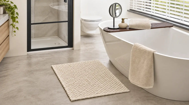 Cremefarbener Badteppich mit strukturierter Oberfläche vor einer weißen Badewanne.