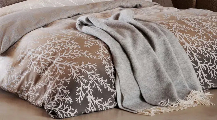 Sofadecken & Wohndecken: Graue Decke mit hellen Fransen auf einem Bett mit taupefarbener, floral gemusterter Bettwäsche