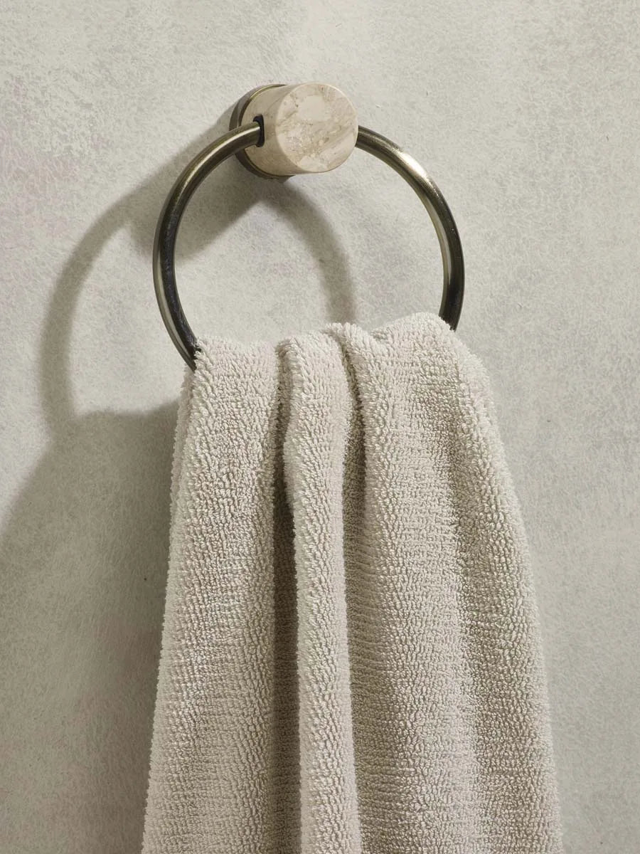 Handtuchring in Bronze mit runder Halterung in heller Steinoptik und beigem Handtuch an einer hellen Wand
