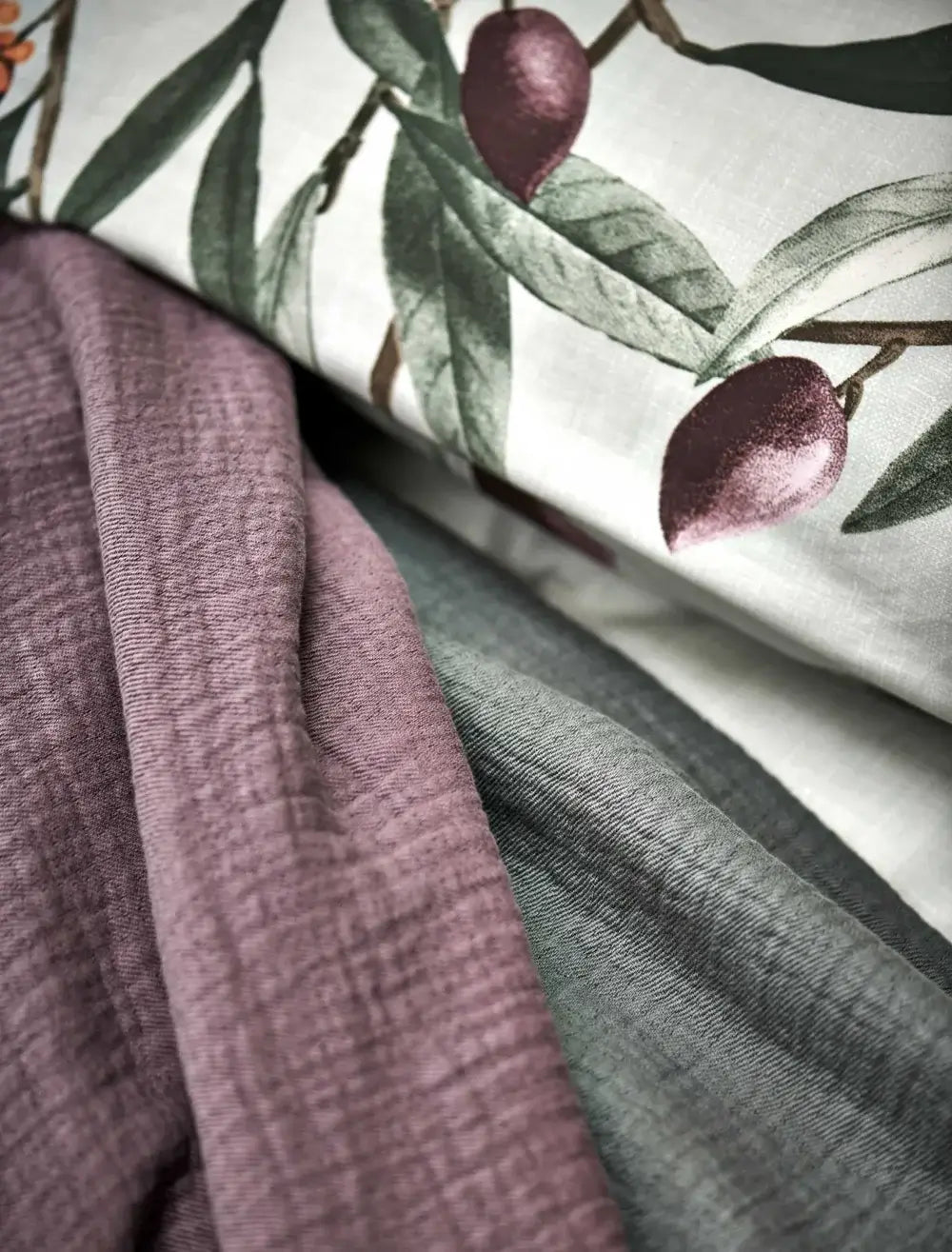 Tagesdecke Vandyck Pure 68, Detail feiner Webstruktur in Violett und Grün neben weißem Stoff mit Olivenmuster
