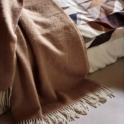 Wolldecke Vandyck Home Bellavita in Mocca, Nahaufnahme des flauschigen Lammwoll-Plaids mit hellen Fransen am Bettrand
