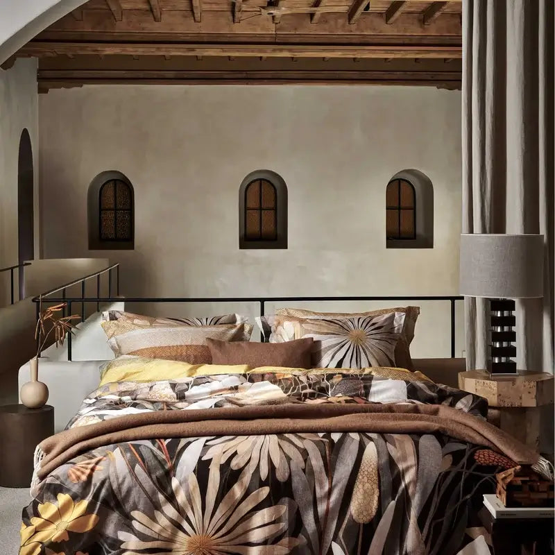 Wolldecke Vandyck Home Bellavita in Mocca, Plaid mit hellen Fransen am Fußende eines Bettes mit großer Blumenmuster-Bettwäsche
